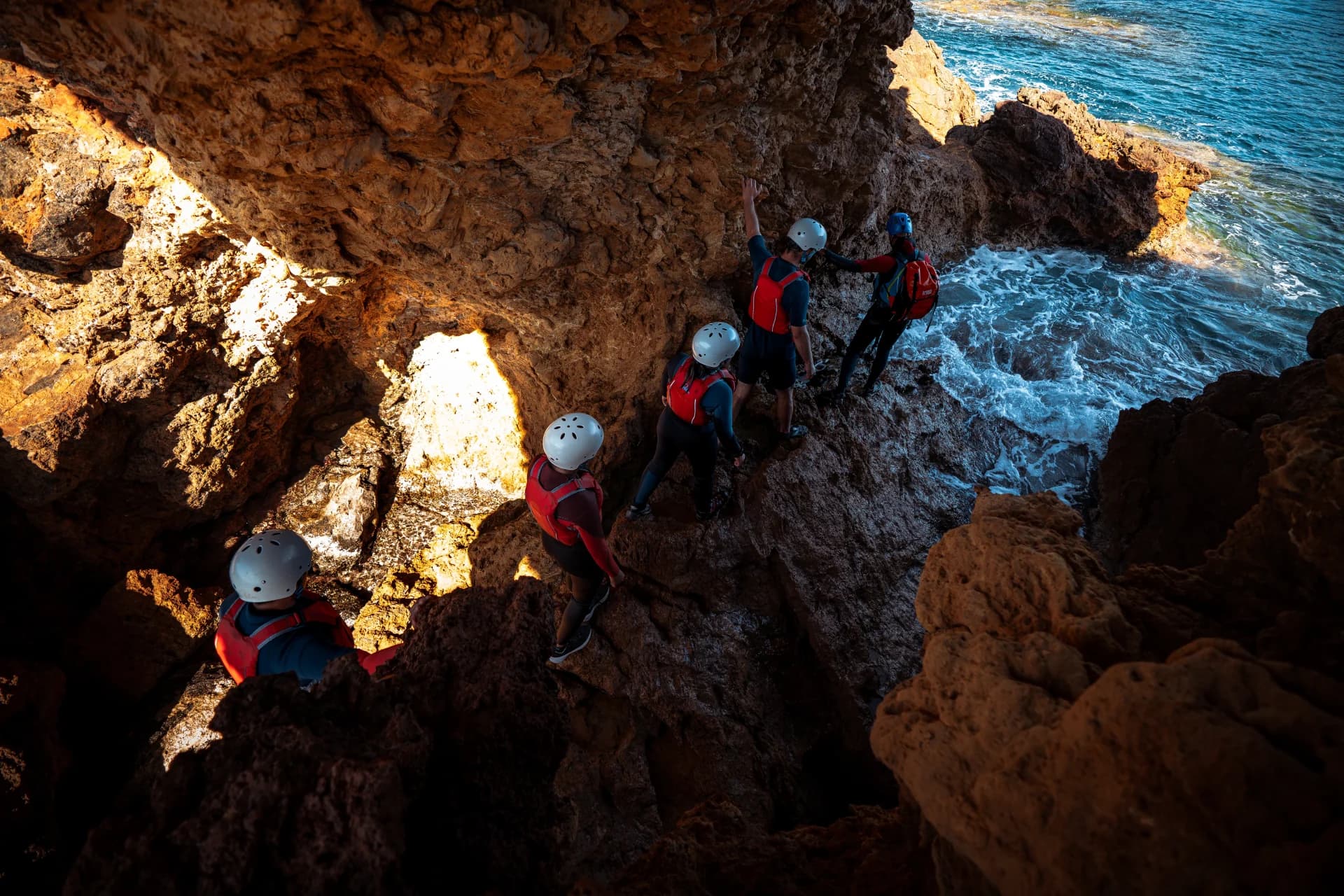 cinco persona caminando entre rocas con sus equipos de coasteering