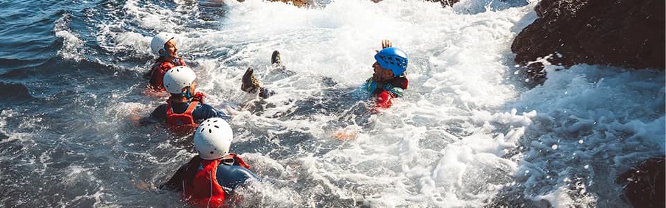 Group of coasteerers swimming through whitewater and waves among rocky coastal formations in Ibiza.